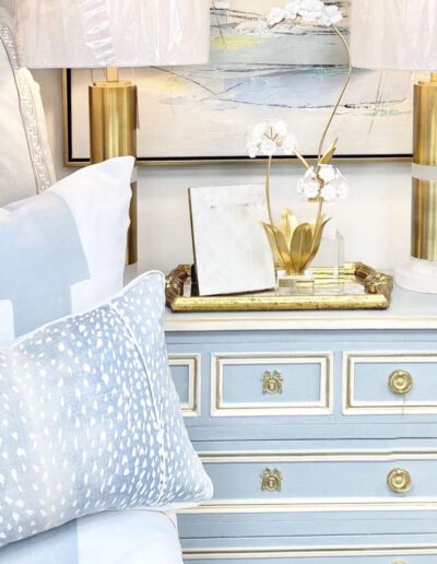 A blue dresser with gold accents and a gold lamp.