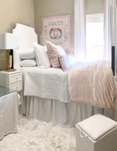 A white and pink dorm room with a bed and dresser.